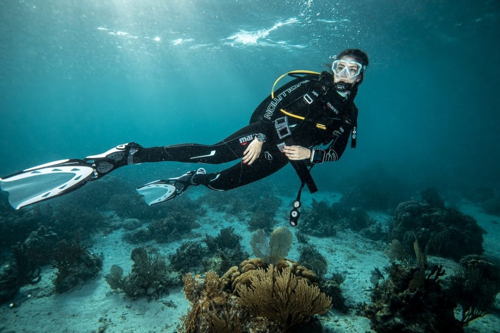 A diver positioned horizontally in the water on a shallow, sandy reef